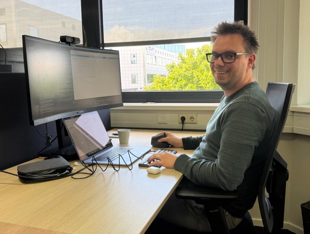Man zit achter laptop en beeldscherm
