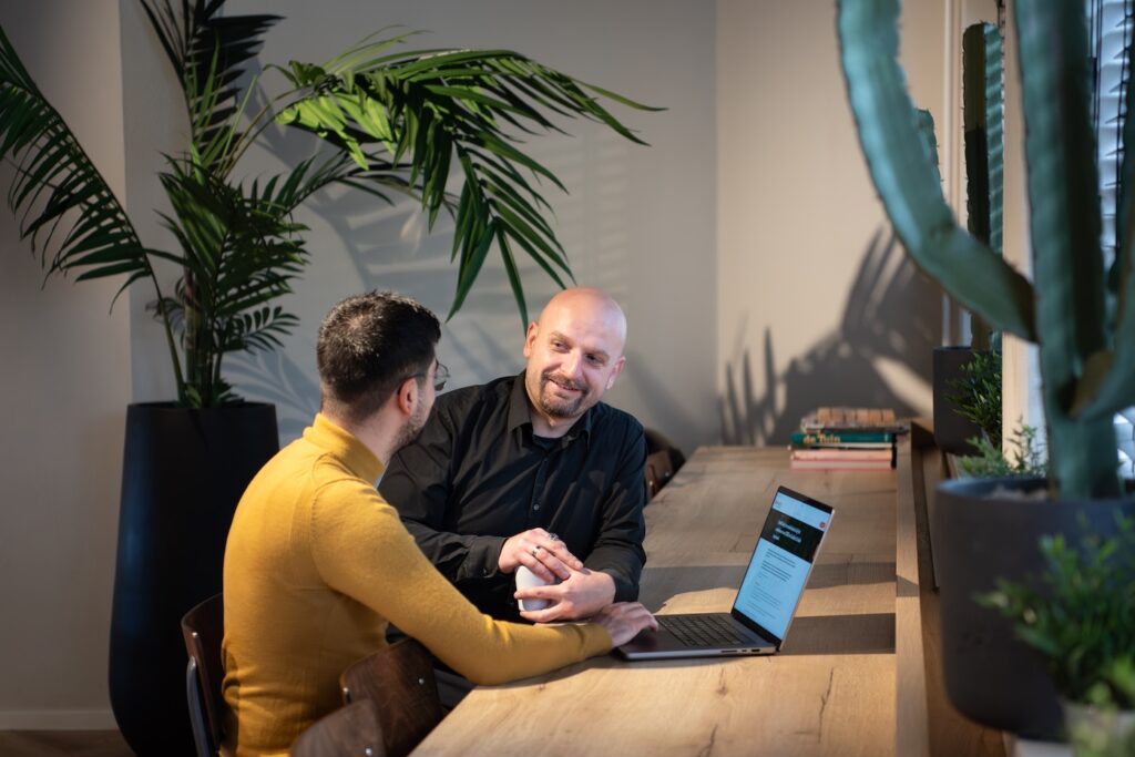 2 talking men around a laptop